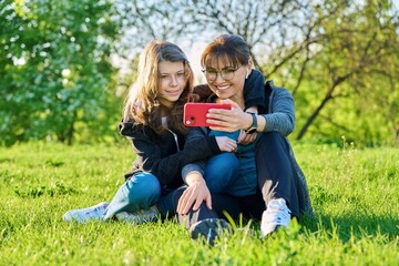 Naklejka na ściany i meble Mom and daughter looking together at smartphone screen, outdoor