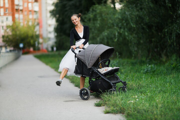cute young european mother walks with gray stroller. baby sleeps in stroller, mom walks in city park in summer