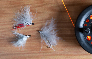 Three fluffy fly fishing flies with a fly reel and orange line