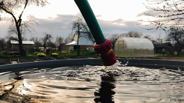 A close-up shot of water flowing from a tap into a large barrel. Shooting close-up in slow motion