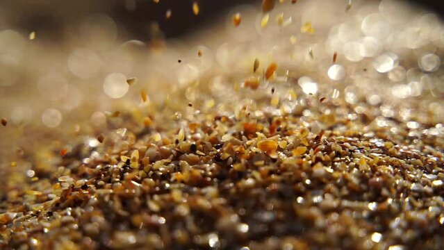 Close-up of sand pouring slowly, against the background of golden bokeh, sunset light. Slow motion.
