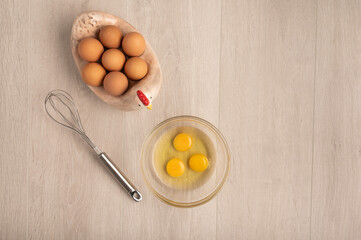 Eggs in a bowl and a whisk on a light wood background