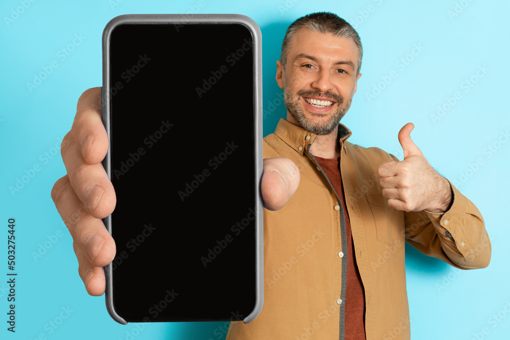 Poster man showing huge cellphone gesturing thumbs up over blue background