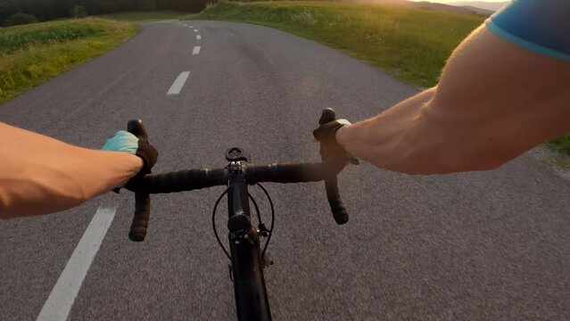 POV Caucasian male athlete riding a racing bicycle on an asphalt road, holding the handlebars tightly with his gloved hands, point of view shot.