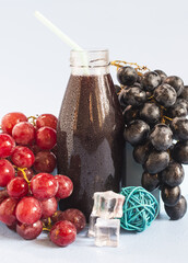 Still life of a vine of dark red and black color and a glass of grape juice on a light background close-up.	