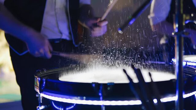 The drummer strikes with sticks on the surface of the drum and splashes fly from it. Shooting close-up in slow motion