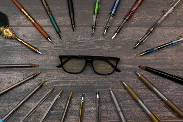 intellectual concept and study. forming an oval of pens, pens, markers surrounding a pair of glasses on a wooden table.