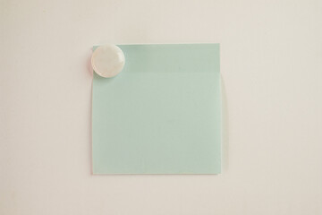Light Blue sticky note with White circle magnet on white wall background.