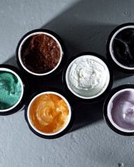 Set with different body scrubs on gray mist, top view. Banner design. Body cream of different colors.