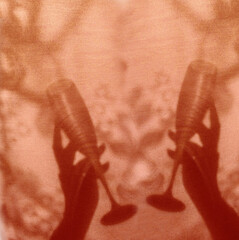 Blurred shadow on shabby red coral wall. Two hands holding wine glass.