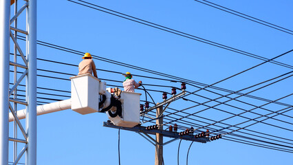 Two electricians on bucket boom truck are installing electrical system on power pole against blue...