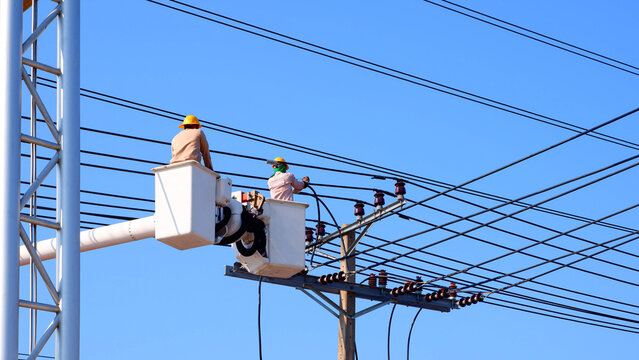 Two electricians on bucket boom truck are installing electrical system on power pole against blue clear sky background