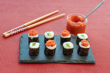 Sushi pieces on a square slate plate, accompanied by red caviar substitute, on a red background.