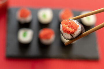 Sushi pieces on a square slate plate, accompanied by red caviar substitute, on a red background.