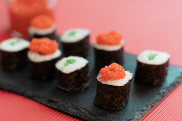 Sushi pieces on a square slate plate, accompanied by red caviar substitute, on a red background.