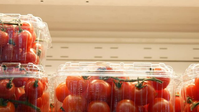 Close-up of many cherry tomatoes in plastic packaging boxes on a fridge shelf and a male hand takes one