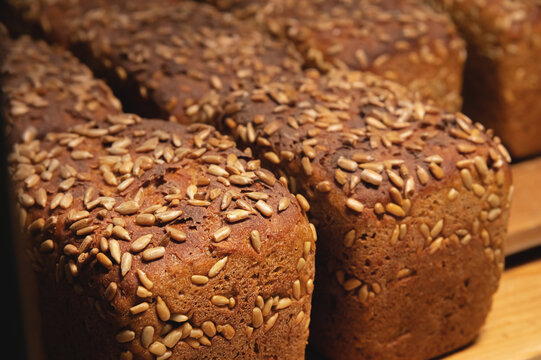 Close-up rye loaves of hot rye bread stand on a wooden tray in a dark bakery room