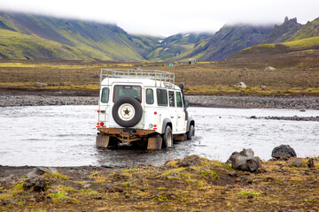 Crossing a tourist jeep car across a mountain river on the road. Stormy mountain river flows from...