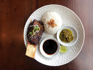 Top view of grilled beef ribs served with white rice, sweet soy sauce and green chili
