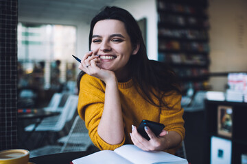 Young cheerful female sitting with hand at chin in cafe