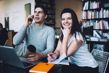 Fototapeta premium Positive young man talking on smartphone during work with colleague