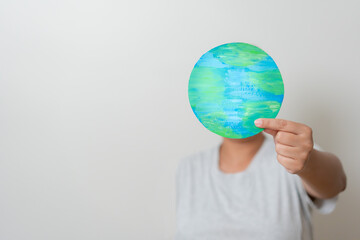 Woman with planet Earth hidden her face. Concept of Earth day, environmental conservation.  Woman holding earth paper cut showing Love and care of the world.