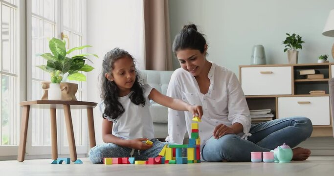 Smart little Indian girl play on warm floor with mom construct from brick set receive praise from parent. Happy preschooler child give high five to mum celebrate success in building fantasy toy castle