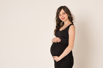Portrait shot of a young beautiful woman in the second trimester of pregnancy on a monochrome background. Close-up of a pregnant woman in casual clothes with her hands on a round stomach. The concept