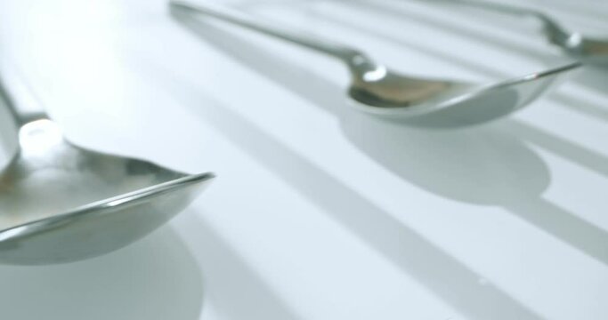 extreme close-up, detailed. large and small stainless steel spoons on a white glossy surface.