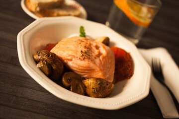 steamed salmon fillet on a pillow of fried mushrooms and tomatoes in a white bowl