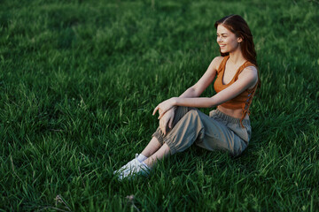 A happy woman looks out at the setting summer sun sitting on the fresh green grass in the park and smiling, view from above. The concept of self-care