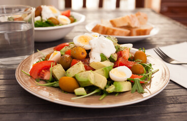 dish of fresh vegetables arugula, avocado, cherry tomatoes with olives on dining table