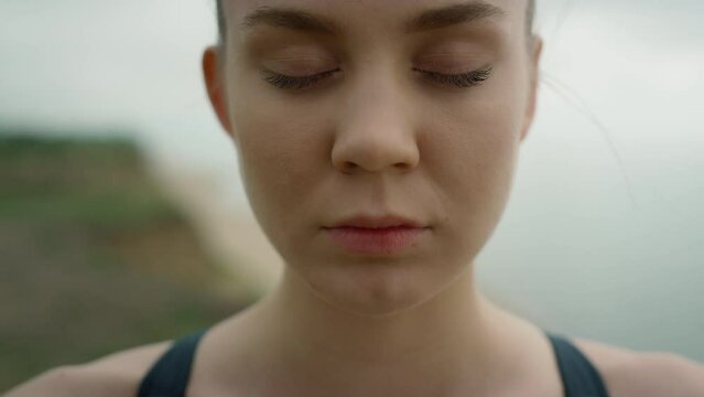 Girl take deep inhale with closed eyes meditating yoga on seashore close up. 
