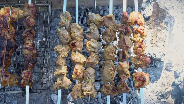 Juicy shish kebab on skewers is fried over a fire and a man turns it over. Grilled meat on an open fire. Picnic in nature, eating outdoors.