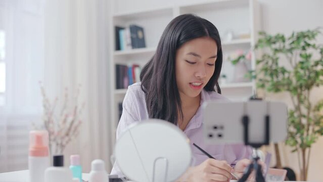 Attractive Asian woman blogger applying makeup, talking with subscribers online