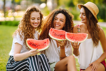 Three young woman  camping on the grass, eating watermelon, laughing. People, lifestyle, travel, nature and vacations concept. Summer concept.