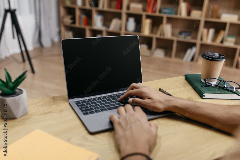 Poster Unrecognizable man working on laptop computer with blank black screen, typing on keyboard, mockup