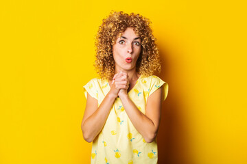surprised shocked curly-haired young woman with wrinkled palms under the chin on a yellow background - obrazy, fototapety, plakaty