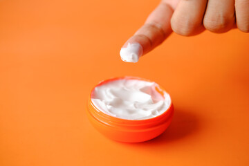 woman applying beauty cream onto skin on orange background 