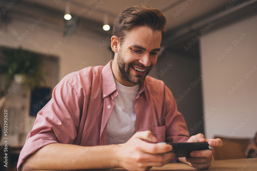 Poster cheerful hipster guy enjoying time for playing virtual 3d via nintendo console joystick while waitin