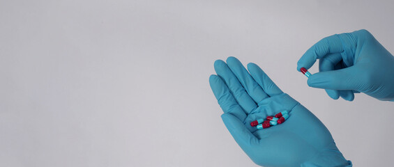 Taking or holding medication pills in hand. Capsule pill on white background isolated. Nitrile disposable gloves and medicines. Drugs healthcare treatment and supplement relieve symptoms of COVID 19.