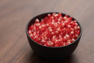 pomegranate seeds in a black bowl on walnut table