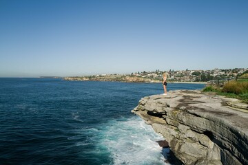 Side view of a woman standing on the cliff overlooking the ocean