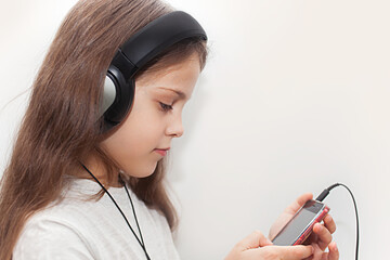 A cute little girl listening to music on a smartphone, black headphones and a gray T-shirt.