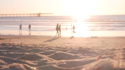 People walking on sandy Ocean Beach by pier at sunset, California coast, USA. Unrecognizable...