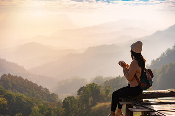 Happy young woman traveler drinking coffe, relaxing and looking at the beautiful sunrise on the top...