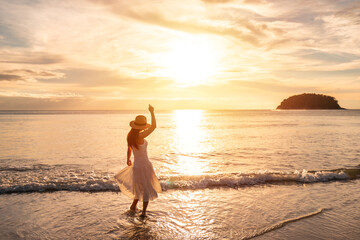 Young woman traveler dancing and enjoying beautiful Sunset on the tranquil beach, Travel on summer...
