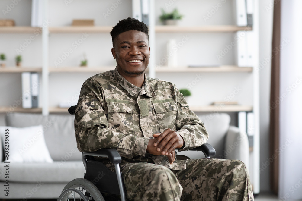 Wall mural Positive african american military man sitting in wheelchair, clinic interior