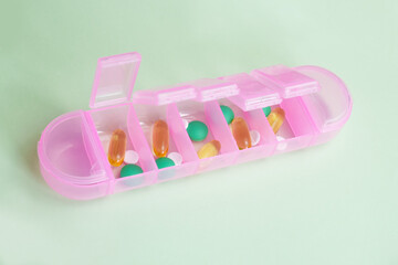 Pink plastic organizer for pills and vitamins on a light green background. Planning for taking medications. Tablets and capsules in a waterproof portable container.