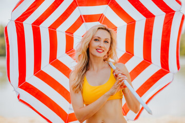 Young attractive blond haired woman in yellow summer bikini posing with bir red and white stripped...